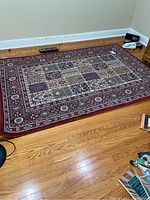 Full view of the rectangular area rug on hardwood floor, showing patchwork design in burgundy, beige and muted blue tones
