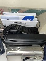 Silver Nikon Coolpix S220 digital camera partially visible with black camera case and Olympus manuals behind