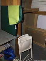 Vintage green card table with quilted table cover stacked against shelving.