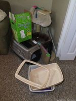 Photo of pet kennel, litter boxes, carpeted scratching posts and cat toys arranged on carpeted floor near corner of room.
