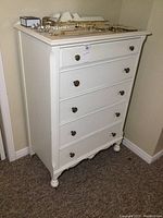 Front angle view showing dresser with five drawers and metal knob handles. Jewelry on top not included.