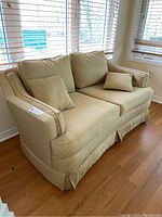 Front view of beige upholstered two-seater loveseat with skirting, featuring square pattern fabric and three pillows.