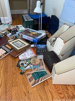 Overview photo of desk and table showing white desk lamp, hanging file trays, games, books, puzzle, binders, and small miscellaneous items scattered on table