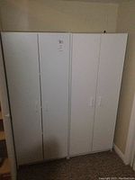 Front view of two white melamine pantry cabinets placed side by side showing two doors on each cabinet.