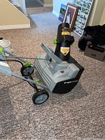 Side view of Earth Wise electric snow thrower showing wheels, handles, and rotating blade housing