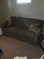 Full view of olive green sofa bed with two patterned cushions against wall