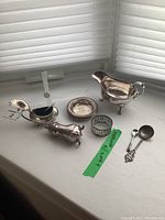 Photo showing the sauce boat, salt dish, napkin ring, commemorative sugar shell spoon, pepper shaker with broken foot, and three small ashtrays all placed on a white surface.