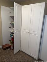 Overall view of two white cabinets side by side with doors closed and one door open showing interior
