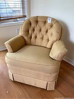 Front view of beige low back upholstered arm chair with tufted back and skirted base.