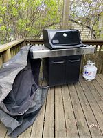 Full view of grill on deck with cover draped and propane tank visible