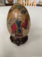 Front side of the hand painted Japanese egg showing a traditional figure in colorful robes holding a fan or circular item.