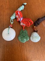 Three jadeite pendants displayed on wooden surface, showing colors and cord attachments.