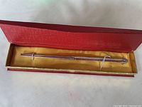 Pair of silver chopsticks displayed inside an open red box with yellow lining