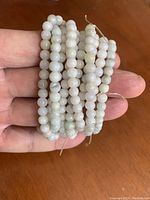 Close up of 5 jadeite bead bracelets being held in hand, showing bead color and size.