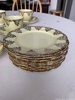 Stack of 9 small plates showing yellow base and gold triangle shaped design with gold edging