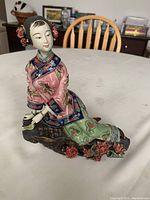 Side angled view of the ceramic Chinese lady figure seated on a dark base, showing floral details on attire and hair accessories.