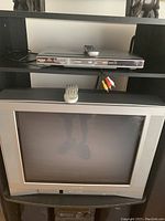Photo showing Toshiba CRT TV with Toshiba DVD player above it on a black shelving unit, includes AV cables and remotes.