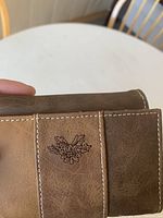 Close-up of the brown tri-tone leather wallet showing detail of floral emboss and stitching.