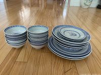 Two stacks of blue and white Chinese porcelain bowls and several stacks of matching plates on wooden floor.