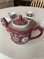 Red porcelain teapot with Chinese longevity symbols and intricate multi-color floral and geometric patterns.