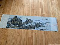 Full view of the silk woven mountain scenery wall hanging laid on wood floor, showing panoramic composition.