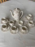 Full set displayed on a table including coffee pot, six cups with saucers, latte mug, sugar mug, and creamer jug.