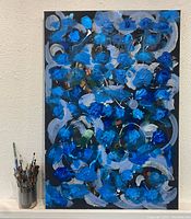 Full vertical view of the large canvas painting with blue and gray abstract patterns on a black background. Container with paintbrushes next to the painting for scale.