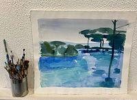 Watercolour painting in plastic cover beside a metal can of artist paintbrushes