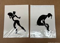 Two drawings in plastic covers shown side by side on brown background