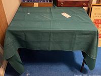 Photo of card table covered with green fabric from front angle showing draped cloth.