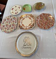 Seven ceramic serving dishes and bowls arranged on a table, floral and geometric patterns, including the silver 25th anniversary plate