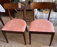 Front view of two chairs showing dark wood curved backrests and pink floral fabric seats.