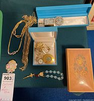 Overview of entire lot showing music box, chains, pocket watch, brooch, and rosary necklace.