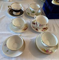 Six tea cups and saucers arranged on a table, displaying various floral designs and gold trim details.