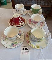 Photo showing all six tea cup and saucer sets arranged on table, featuring various floral patterns and gold trim