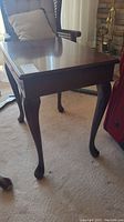 View of the dark stained wooden end table showing the flat top surface, cabriole legs, and part of surrounding furniture.