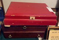 Two stacked red storage cases with visible wear, one including a drawer with brass handles.