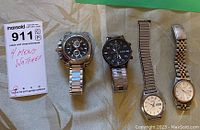 Four men's watches displayed side by side on fabric with label indicating 4 men's watches