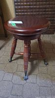 Full view of the wooden piano stool showing the round seat, spindle legs, and claw feet.