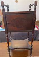 Full view of dark stained wood smoking stand with door and fabric sling bottom shelf, displaying turned wooden legs and slightly worn top surface.