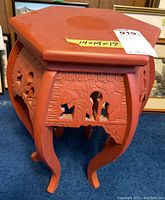 Full view of orange painted wood carved stand with hexagonal top and detailed carvings on sides and curved legs.