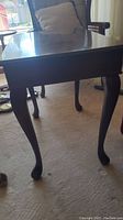 Dark stained wooden end table with a flat rectangular top and cabriole legs placed on a carpeted floor.
