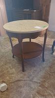 Full view of round occasional table with marble top and wooden base, displayed on carpeted floor.