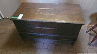 Front view of vintage wooden chest showing ornate carved design and wooden top with some wear.
