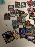 Top view of assorted random trading cards spread on a white table, mostly Yu-Gi-Oh! cards visible.