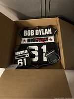 Photo of the collector's box showing a Bob Dylan shield-shaped clock, badge, and pass with Highway 61 design.