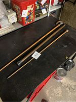 Full view of three walking canes laid out on a black surface with some background storage items visible.