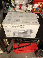 Rowenta Pro Compact garment steamer in its original retail box, placed on a shelf.