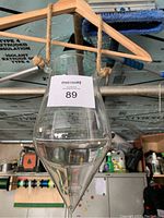 Full view of hanging glass vase suspended from wooden hanger showing clear glass and rope knots.