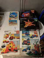 Photo of 4 LEGO instruction booklets featuring various classic sets with cars, planes, helicopters, and buildings.